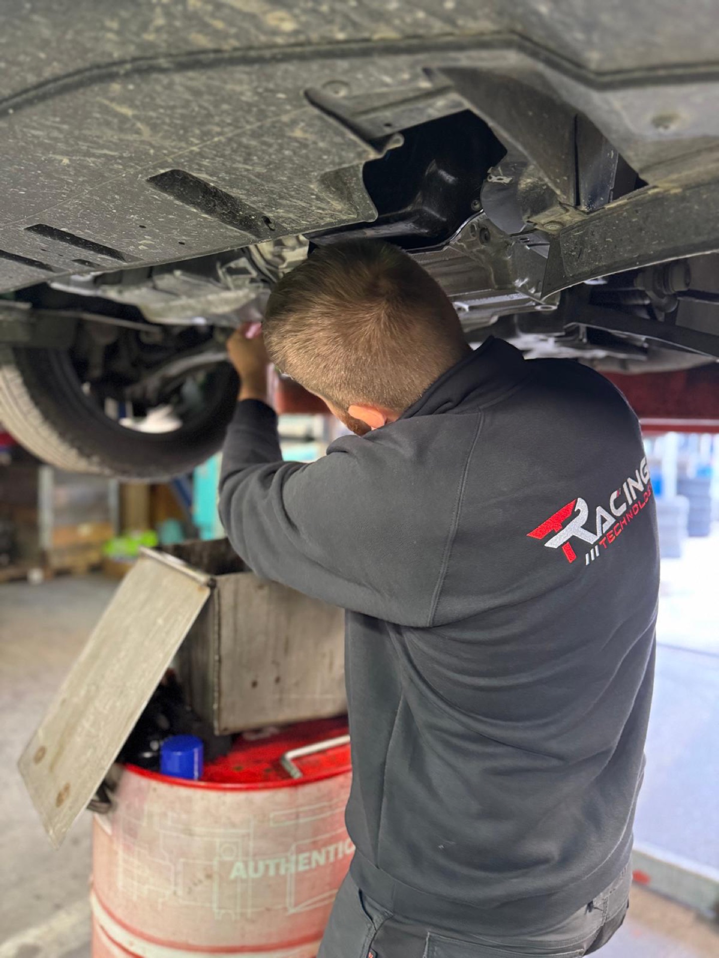 Un mécanicien Racing Technology sous une voiture levée sur le pont de l’atelier de Namêche